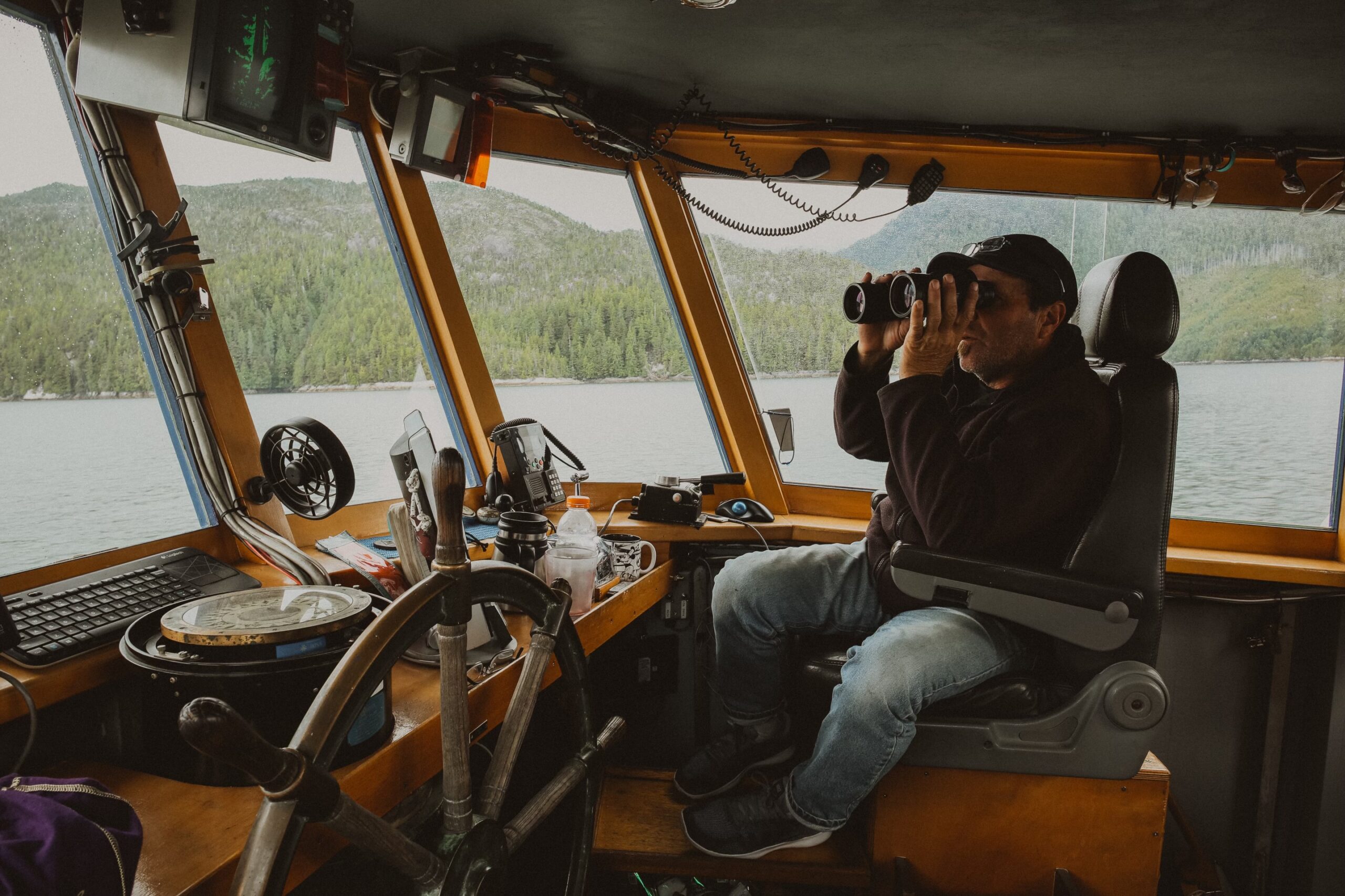 man in boat wheelhouse looking through binoculars